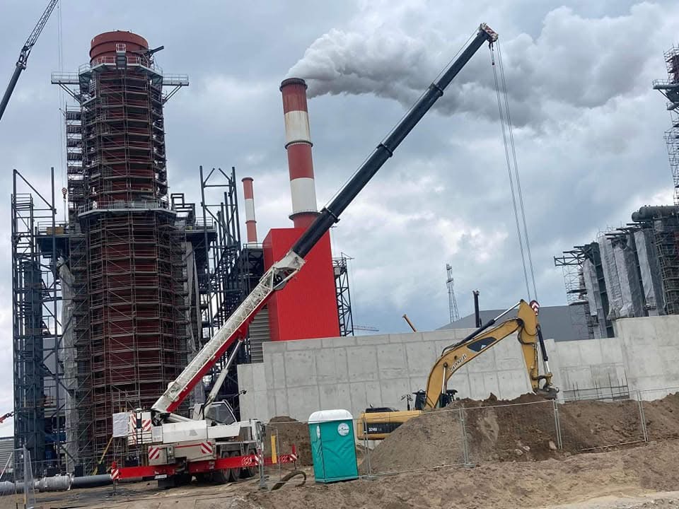Żuraw terenowy na placu budowy zakładu przemysłowego z rozbudowaną infrastrukturą energetyczną i rusztowaniami przy kominie